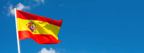Flag of Spain waving in the wind on flagpole against the sky with clouds on sunny day, banner