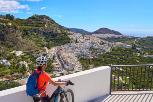 nice senior woman cycling with her electric mountain bike in the picturesque white village of Frigiliana near Nerja, Andalusia, Spain